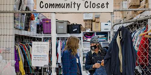 A community clothes closet with two people perusing the clothes on racks and shelves